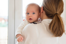 Foto Baby mit blauen Augen schaut über die Schulter seiner Mutter